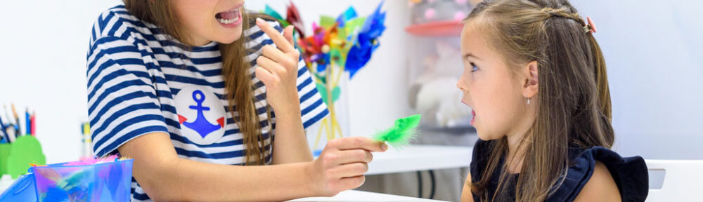 Speech therapist working with young girl blowing feather