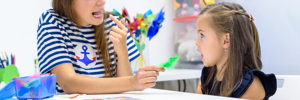 Speech therapist working with young girl blowing feather