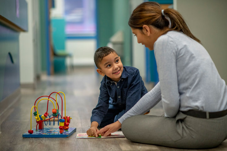 therapist with young hispanic boy playing on the floor
